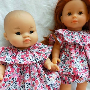Peut inclure: Deux poupées portant des robes à fleurs assorties avec des cols à volants. La poupée de gauche a un teint clair et des cheveux bruns courts. La poupée de droite a un teint clair et de longs cheveux roux.