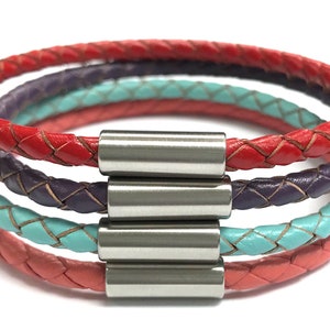 May include: A multi-layered leather bracelet with a braided design. The bracelet is made of four strands of leather in red, pink, turquoise, and purple. The bracelet is secured with a silver magnetic clasp.
