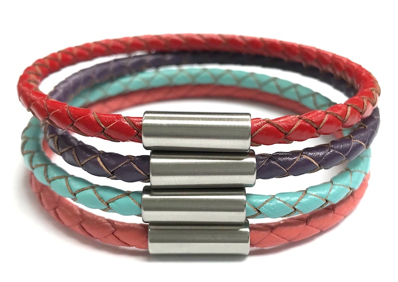 May include: A multi-layered leather bracelet with a braided design. The bracelet is made of four strands of leather in red, pink, turquoise, and purple. The bracelet is secured with a silver magnetic clasp.