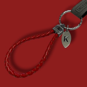 May include: Red braided leather keychain with a silver key ring and a silver charm with the letter K.