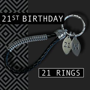 May include: A black leather keychain with a silver metal ring and two silver charms. The charms are engraved with "21" and "W". The text "21ST BIRTHDAY" and "21 RINGS" are displayed in white.