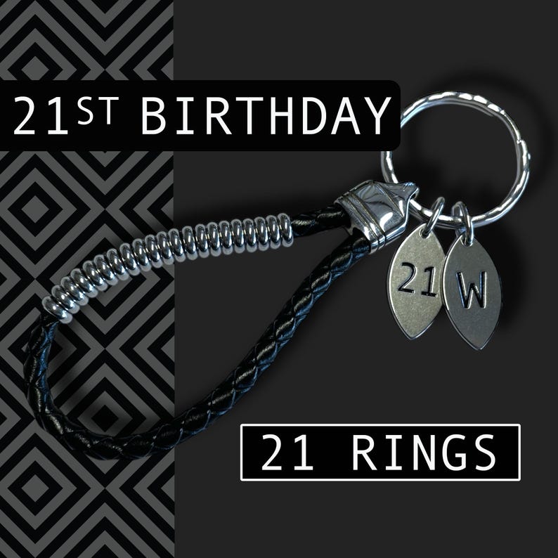 May include: A black leather keychain with a silver metal ring and two silver charms. The charms are engraved with "21" and "W". The text "21ST BIRTHDAY" and "21 RINGS" are displayed in white.