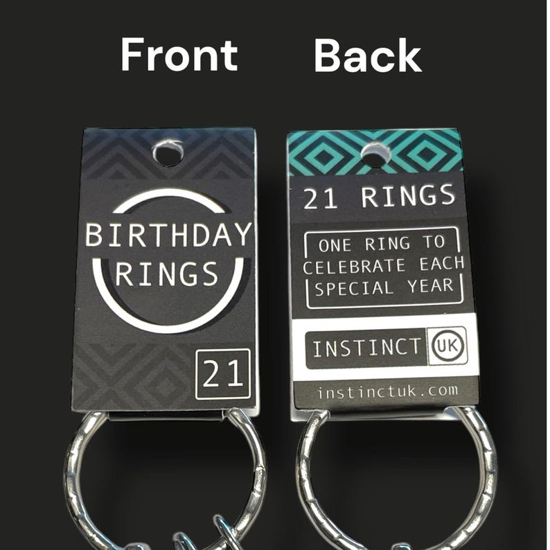 May include: A set of 21 rings on a keychain, with a black and white tag. The front of the tag reads "BIRTHDAY RINGS" and "21". The back of the tag says "21 RINGS" and "ONE RING TO CELEBRATE EACH SPECIAL YEAR".