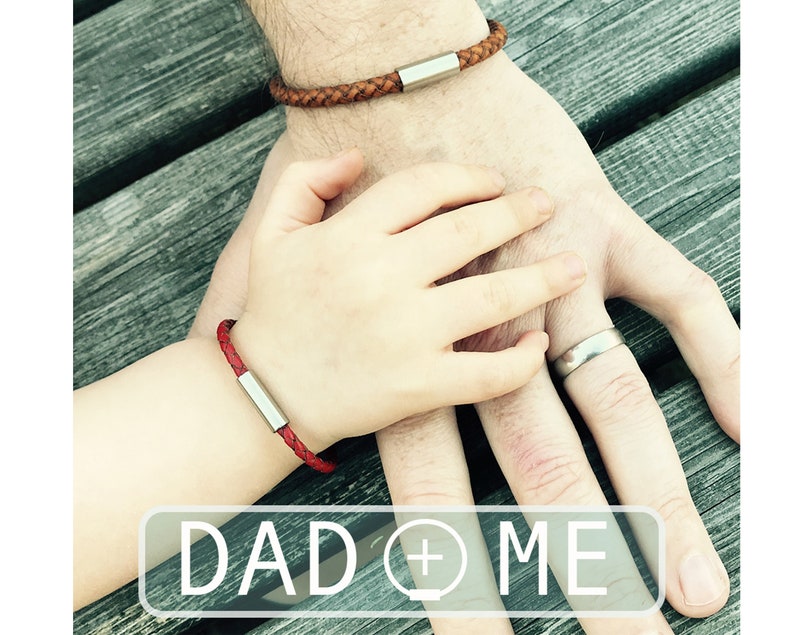 Puede incluir: Dos personas llevando pulseras de cuero a juego con detalles plateados. Las pulseras son trenzadas y tienen un dise&ntilde;o sencillo. El texto "DAD + ME" es visible en la imagen.