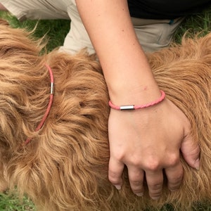 May include: A pink leather bracelet with a silver clasp. The bracelet is worn on a person's wrist.