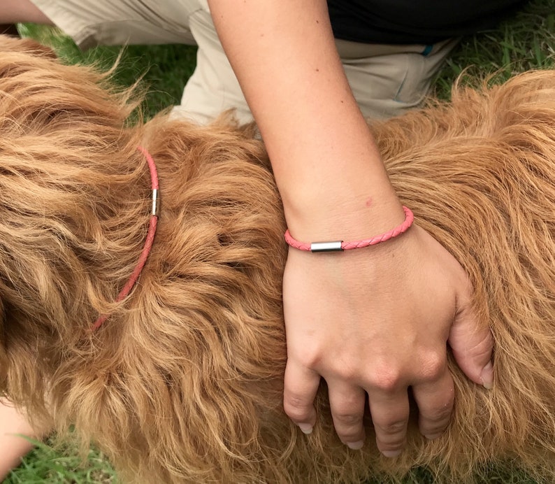 May include: A pink leather bracelet with a silver clasp. The bracelet is worn on a person's wrist.