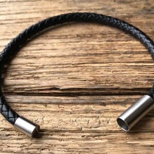 May include: A black leather bracelet with a braided design and silver metal clasps.