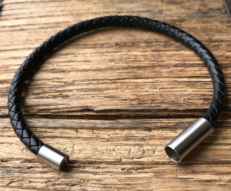 May include: A black leather bracelet with a braided design and silver metal clasps.