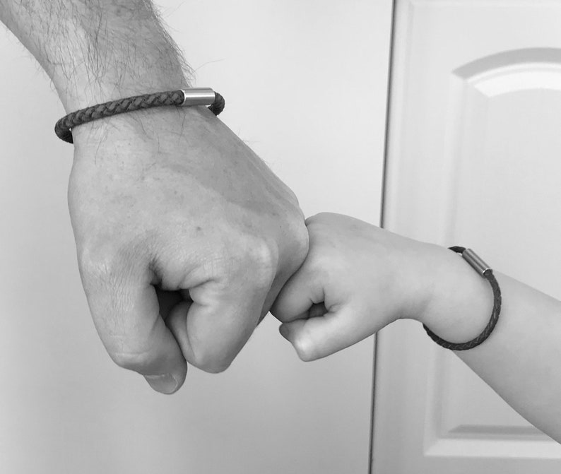 Puede incluir: Dos personas, una con una pulsera de cuero negro con un cierre plateado, se dan un pu&ntilde;etazo. La pulsera en la mu&ntilde;eca m&aacute;s peque&ntilde;a tiene un cierre plateado m&aacute;s peque&ntilde;o.