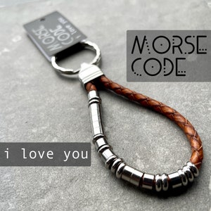 May include: A brown leather keychain with a silver metal ring and a silver metal chain of beads. The keychain has a small tag that says "Morse Code I Love You".