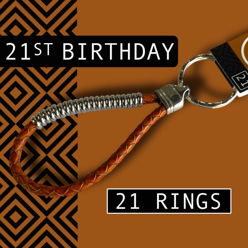 May include: A brown leather keychain with a silver metal accent and a silver key ring. The keychain has the text "21ST BIRTHDAY" and "21 RINGS" on a brown background with a black and orange geometric pattern.
