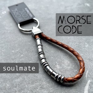 May include: A brown leather keychain with a silver metal ring and a series of silver beads. The keychain has the words "MORSE CODE" printed on it. The word "soulmate" is printed on a black tag.