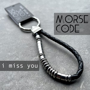 May include: Black leather keychain with a silver metal ring and a silver metal chain of beads that spell out "I miss you" in Morse code. The keychain has a tag that says "Morse Code I Miss You".