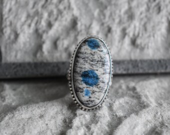 May include: A silver ring with a blue and white oval-shaped stone set in a silver bezel. The stone has a speckled pattern with blue and white swirls.