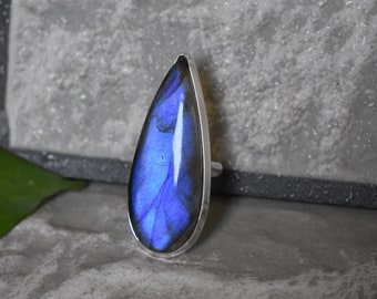May include: A teardrop-shaped ring with a blue labradorite gemstone set in a silver band.
