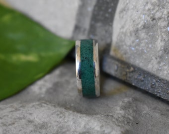 May include: A silver ring with a green inlay. The ring is a simple band with a thin strip of green material set into the metal.