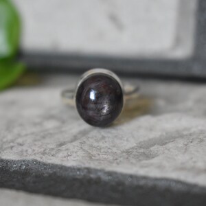 May include: A silver ring with a dark gray oval gemstone. The gemstone has a shimmery, iridescent quality.
