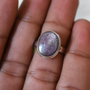 May include: A silver ring featuring a purple oval gemstone. The gemstone has a star-like pattern.