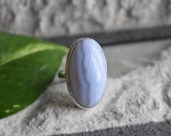 May include: A silver ring with a large oval blue agate gemstone. The stone has a swirling pattern of light and dark blue.