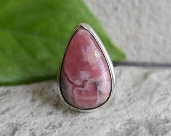 Puede incluir: Un anillo en forma de lágrima con una piedra preciosa rosa y blanca engastada en una banda de plata.