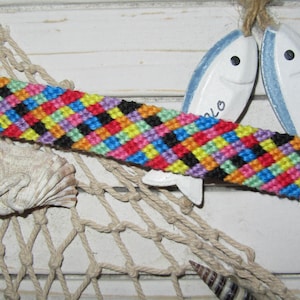 Peut inclure: Un bracelet d'amitié coloré avec un motif à carreaux en noir, rouge, orange, jaune, vert, bleu, violet et rose.