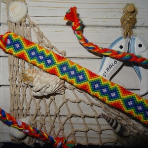 Peut inclure: Un bracelet d'amitié coloré avec un motif arc-en-ciel et un design en chevron. Le bracelet est fait de plusieurs couleurs, dont le rouge, l'orange, le jaune, le vert, le bleu et le violet. Le bracelet est noué à l'extrémité.