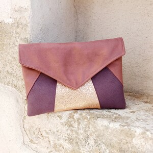 Puede incluir: Un bolso de mano marrón, morado y dorado con un diseño geométrico. El bolso tiene un cierre de solapa y una cremallera dorada.