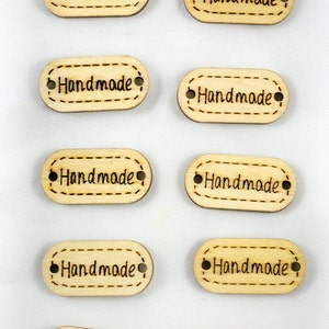 Peut inclure: Dix étiquettes ovales en bois avec le mot "Handmade" écrit dessus. Chaque étiquette a deux trous pour une ficelle ou un ruban.