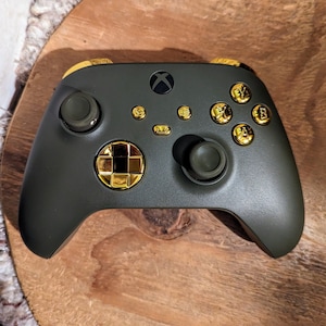May include: A dark green Xbox controller with gold buttons and a gold faceplate. The controller has a textured grip and a standard layout.