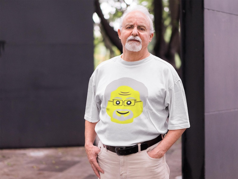 May include: A white t-shirt with a yellow cartoon face of a man with gray hair and glasses. The man is smiling.
