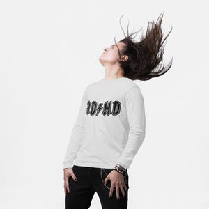 Person wearing a white long-sleeve shirt with bold black AD HD design, flipping hair back — fun ADHD SVG for shirts with rock band vibe.