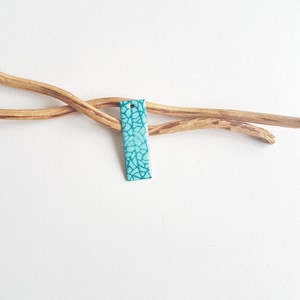 Può includere: Un'etichetta rettangolare di colore turchese con un motivo bianco e turchese. L'etichetta ha un foro nella parte superiore per appenderla.