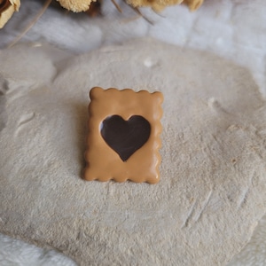 Peut inclure: Un biscuit brun avec un découpage en forme de cœur rempli de chocolat brun foncé. Le biscuit est sur une surface brun clair.