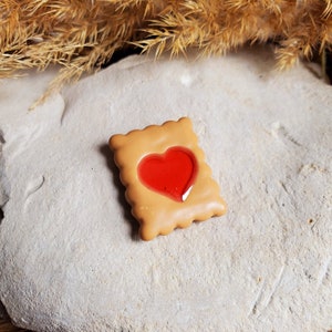 Peut inclure: Un biscuit brun avec une garniture de gelée rouge en forme de cœur. Le biscuit est décoré d'un bord festonné.