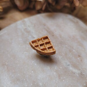 Peut inclure: Une petite gaufre brune en pâte polymère. La gaufre est posée sur une surface blanche.