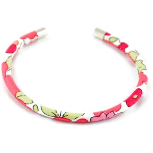 May include: A white headband with a floral pattern in shades of pink and green. The headband is made of fabric and has metal ends.