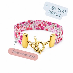 Peut inclure: Bracelet en tissu à motif floral rose et rouge sur fond blanc. Il est doté d'un fermoir à bascule doré. Le texte "Personnalisable" est visible. Le texte "+ de 300 tissus" est également visible.