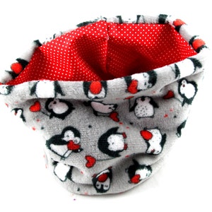 Peut inclure: Un snood en polaire grise avec un motif de pingouins et une doublure à pois rouges. Les pingouins ont des corps noirs et blancs avec des accents rouges. L'écharpe est douce et moelleuse.