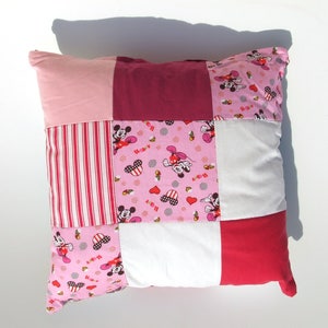 Peut inclure: Un oreiller patchwork rose, rouge et blanc avec un imprimé Mickey Mouse et Minnie Mouse. L'oreiller est fait de différents tissus et présente une variété de couleurs et de motifs.