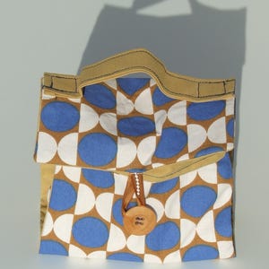 Peut inclure: Un sac à déjeuner brun et blanc avec un motif géométrique bleu. Le sac a une poignée en cuir brun et une fermeture à bouton brun.