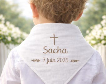 May include: A white triangular bandana worn around the neck, featuring brown embroidery of a cross, the name Sacha, and the date 7 juin 2025, accented by small leaf motifs. The fabric is plain white, and the design is centered on the back.