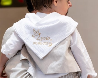 May include: A white muslin triangular scarf featuring gold embroidery of a dove, a cross, the name Lyvio, and the date 09/06/2024. The scarf is worn over a white long-sleeved shirt and a beige vest with light brown striped trousers.