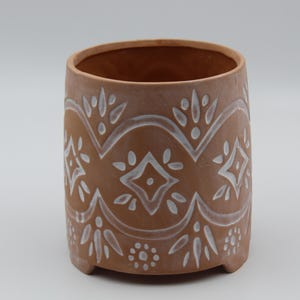 May include: A terracotta planter with a white geometric design. The planter has a rounded base and a wide opening.