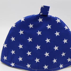 May include: A blue fabric tea cosy with white stars. The cosy has a loop on top for hanging.