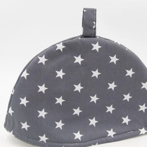 Può includere: Scaldabiberon grigio con un motivo a stelle bianche e un manico ad anello.