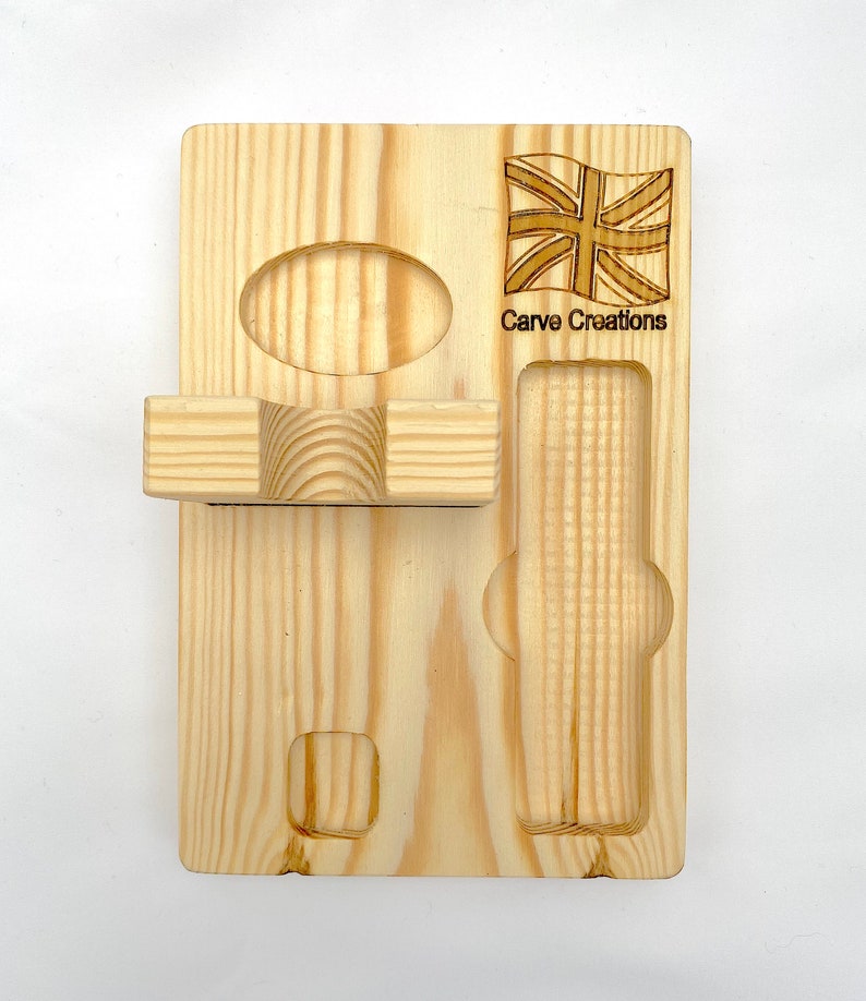 Puede incluir: Un organizador rectangular de madera clara con una bandera Union Jack grabada y el texto Carve Creations. La tabla incluye un estante horizontal, una hendidura circular, una ranura rectangular y un peque&ntilde;o recorte cuadrado para almacenamiento.