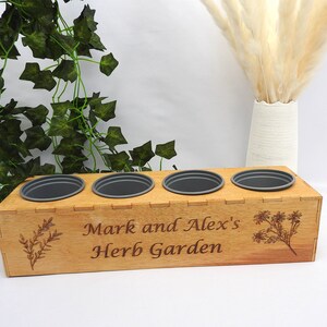 May include: Wooden planter box with four grey pots, engraved with the text "Mark and Alex's Herb Garden" and a floral design.