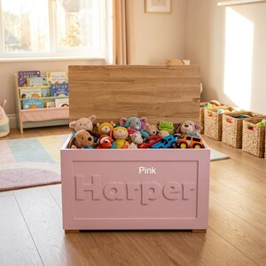 May include: A pink wooden toy chest with a natural wood lid, featuring the name Harper embossed in large letters on the front. The chest is filled with various plush stuffed animals and small toy vehicles, providing storage for children's play items.