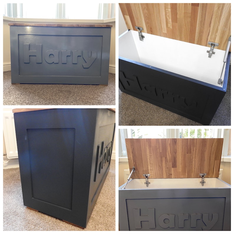 May include: A rectangular storage chest with a dark gray exterior and a natural wood grain lid. The front panel features the name Harry in raised lettering. The interior is white, and the lid is attached with metal hinges and a gas strut.
