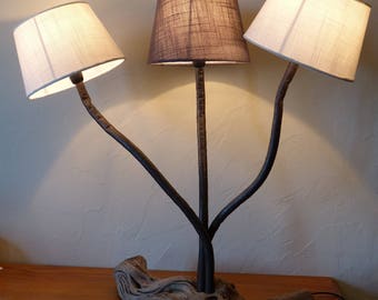 Lampe composée d'un pied en bois flotté , de tiges en métal rouillé en mer  verni et de trois abat-jours en tissu , 2 blancs et 1 taupe